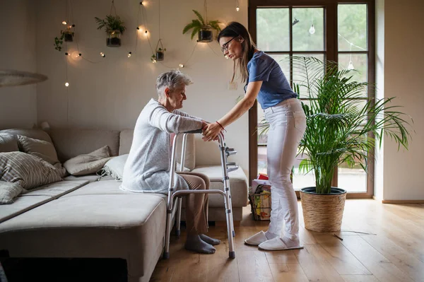 Vista laterale dell'operatore sanitario o del badante che visita una donna anziana in casa, aiutandola a camminare. — Foto Stock