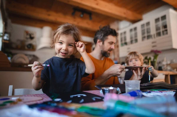 Padre maturo con due bambini piccoli che riposano in casa, dipingendo quadri. — Foto Stock