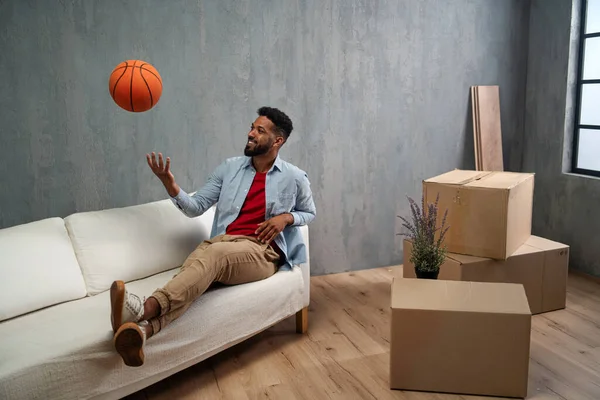 Joyeux jeune homme avec basket célébrant le déménagement entouré de boîtes d'emballage, nouveau concept de vie. — Photo
