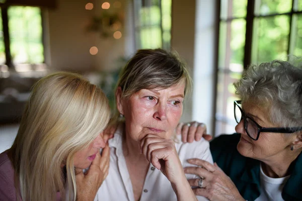 Female senior friends consloing and supporting sad friend indoors at home. — Stock Photo, Image