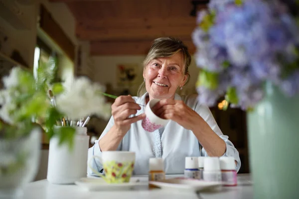 Low angle view of happy senior artist woman painting cermaic cup, artcraft concept. — Stock Photo, Image