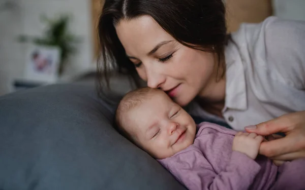 Joyeux jeune mère embrasser son nouveau-né fille, couché sur le canapé à l'intérieur à la maison. — Photo