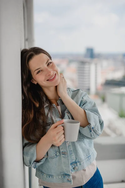 Porträt einer jungen kaukasischen Frau mit Kaffee im Freien auf dem Balkon und Blick in die Kamera. — Stockfoto
