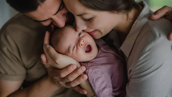 Evde yeni doğmuş bebeklerini kucaklayan ve öpen genç ebeveynlerin yakın çekimi. — Stok fotoğraf