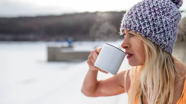 Ritratto di donna anziana attiva in abiti sportivi che beve tè all'aperto in inverno, concetto di terapia fredda. Copia spazio. — Foto Stock