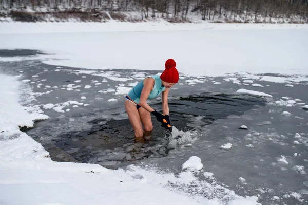 Mayo giymiş, kışın dışarıda baltayla buz kıran aktif yaşlı bir kadın. Soğuk terapi konsepti.. — Stok fotoğraf
