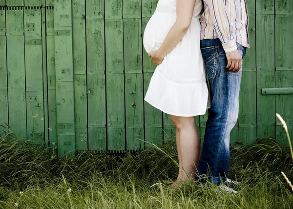 Беременная пара перед зеленым забором — стоковое фото