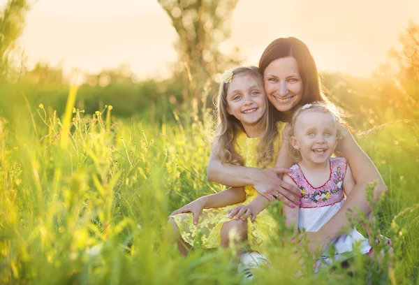 Glad mamma med döttrar i solig äng — Stockfoto