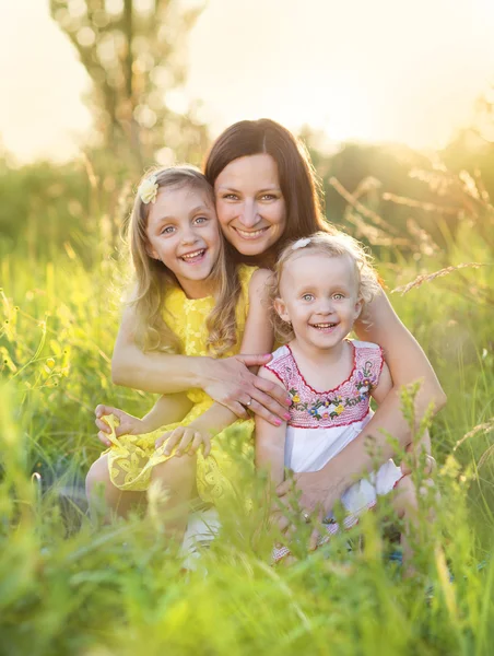 Glad mamma med döttrar i solig äng — Stockfoto