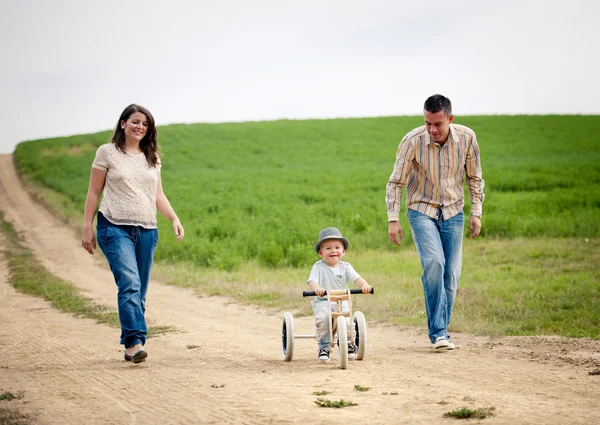 Üç tekerlekli bisiklet yürüyüş üzerinde küçük çocuk ile aile — Stok fotoğraf
