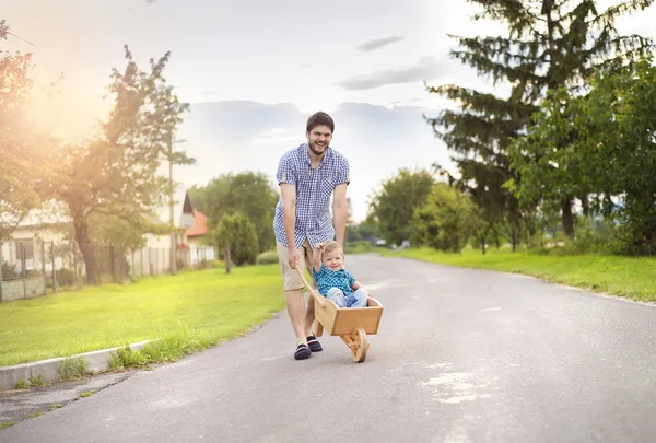 Vater schiebt seinen Sohn in Holzschubkarre — Stockfoto