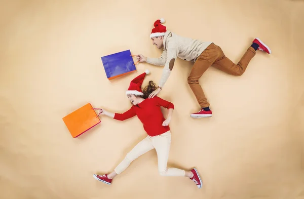Couple in Christmas hats running with shopping bags — Stock Photo, Image