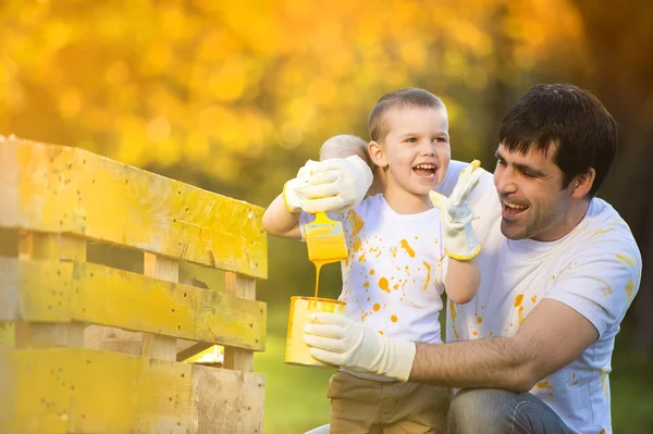 Мальчик и его отец красили деревянный забор — стоковое фото
