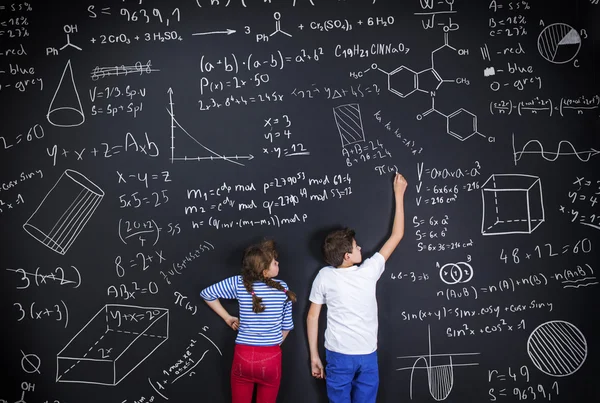 Garçon et fille apprenant devant un tableau noir — Photo