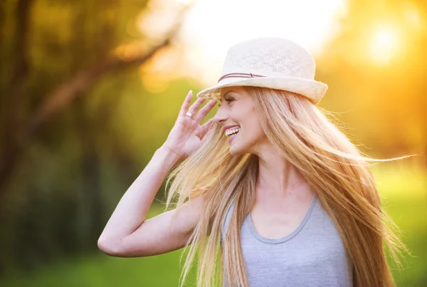 Kobieta w białym kapeluszu śmiejąc się w słoneczny park — Zdjęcie stockowe