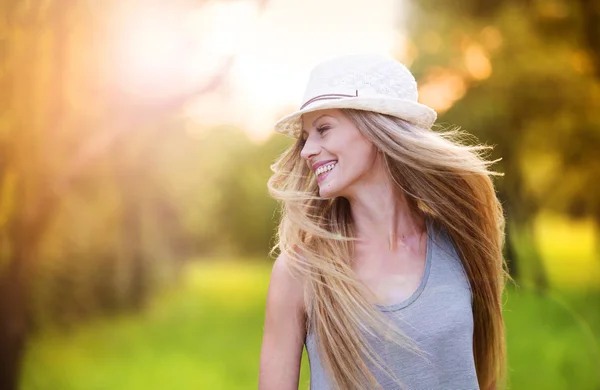 Жінка в білому капелюсі сміється в сонячному парку — стокове фото