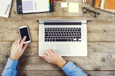 Dizüstü bilgisayar ve cep telefonu kullanan adam elinde.