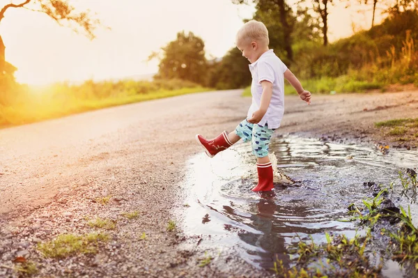 Küçük çocuk bir su birikintisine oynarken — Stok fotoğraf