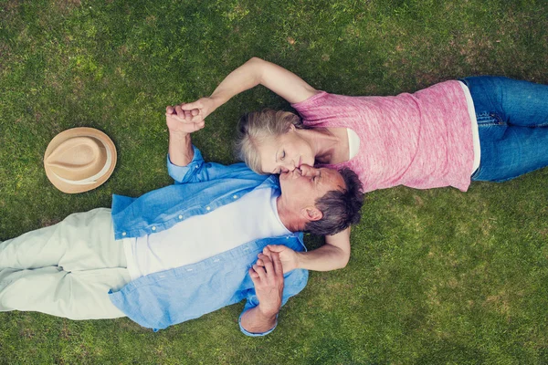 Senior paar liggen op een gras en knuffelen — Stockfoto