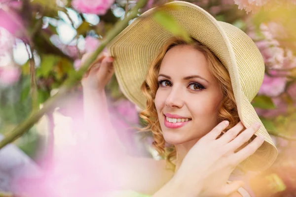 Woman in hat posing in pink flowers — Zdjęcie stockowe