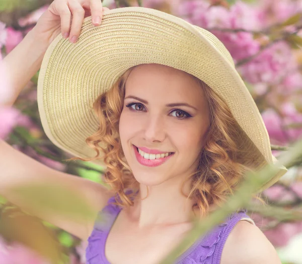 Woman in hat posing in pink flowers — Stok fotoğraf