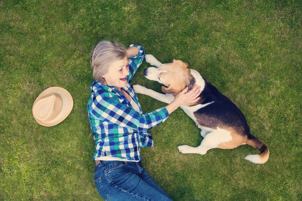 Seniorin mit Hund im Gras liegend — Stockfoto