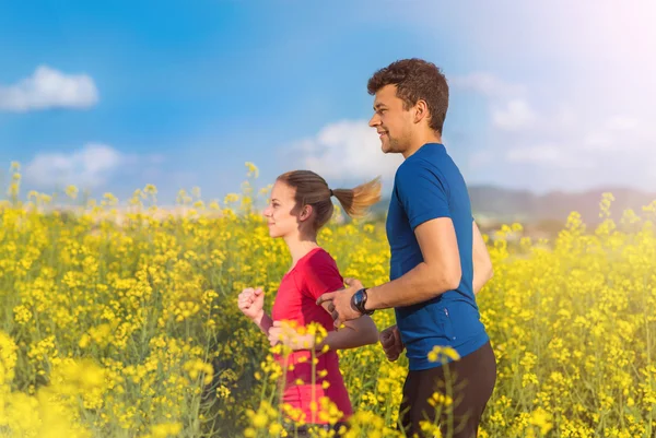 Couple running in spring canola field — Stock Photo, Image