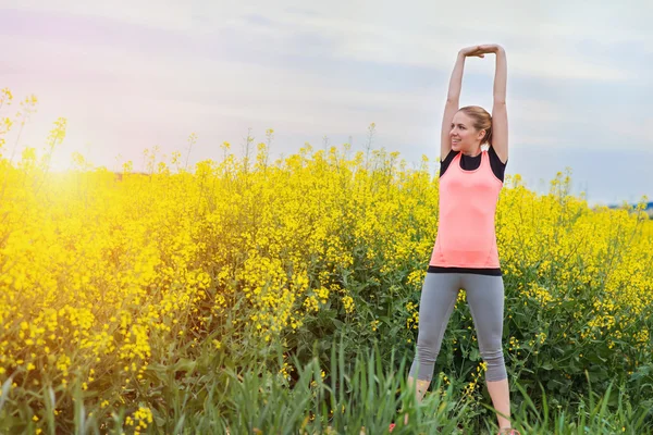 Woman stretching in spring canola field — Stock Photo, Image