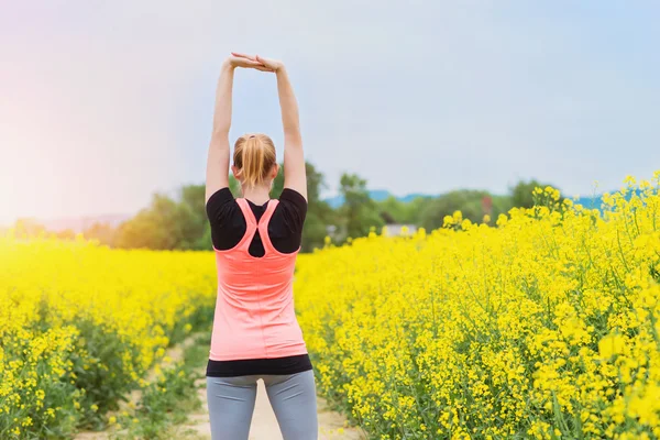 Woman stretching in spring canola field — Stock Photo, Image