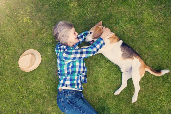 Senior mujer con su perro acostado en una hierba — Foto de Stock