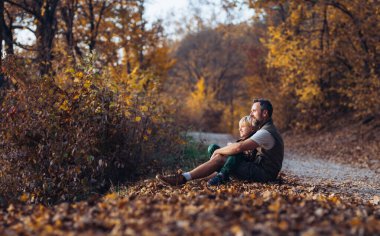 Baba ve oğul sonbahar doğasında, dökülen yaprakların üzerinde oturuyorlar. Hindistan yaz konsepti.