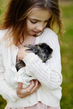 Genç bir kız nazikçe kollarında tüylü bir tavşana sarılıyor..