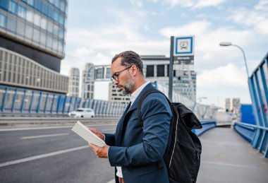 Yetişkin bir adam otobüs beklerken kitap okuyor. Kentsel banliyö.