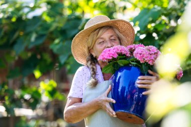 Bahçede elinde pembe çiçeklerle gülümseyen bahçıvan.