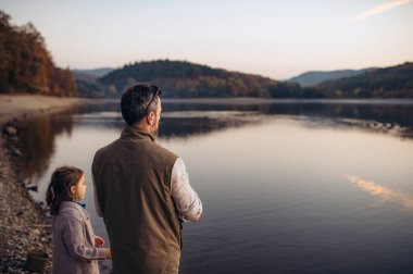 Baba ve kızı sıcak bir sonbahar akşamı göle bakıyorlar. Hindistan yaz konsepti.