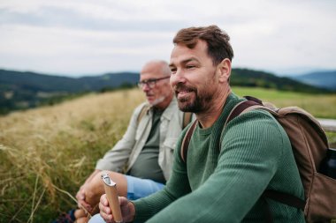 Olgun oğul ve babası sonbahar doğasında yürüyüş yaparken bir yudum alıyorlar..