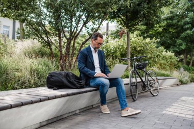 Şehir parkında çalışan bir yönetici, dizüstü bilgisayarda çalışıyor. Yanında bisiklete bin..