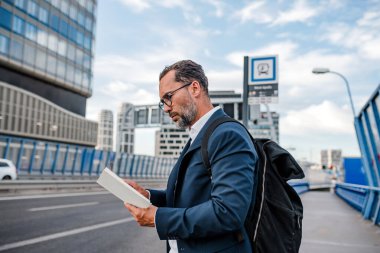 Yetişkin bir adam otobüs beklerken kitap okuyor. Kentsel banliyö.