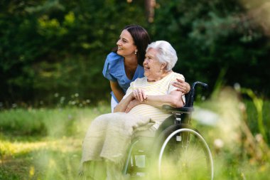 Tekerlekli sandalyede yaşlı bir hastayla yürüyen kadın hemşire..