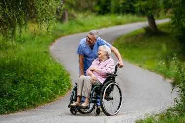 Tekerlekli sandalyedeki yaşlı hastayla yürüyen erkek hemşire..