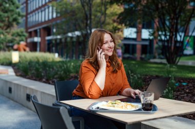Kafede uzaktan çalışan kıvrımlı bir kadın müşterisiyle telefon görüşmesi yapıyor..