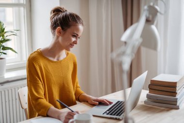 Masada oturan ve ders çalışan kız öğrenci..