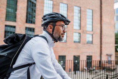 Kasklı ve sırt çantalı bir adam işe bisikletle gidiyor.