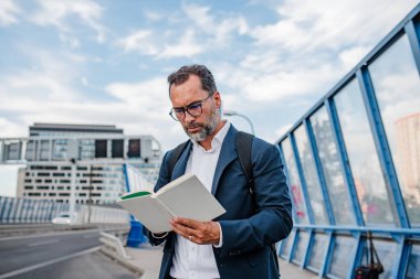 Yetişkin bir adam otobüs beklerken kitap okuyor. Kentsel banliyö.