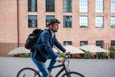 Kasklı ve sırt çantalı bir adam işe bisikletle gidiyor.