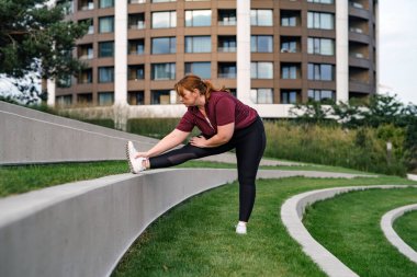 Vücut pozitifliği olan kadın antrenmandan önce ısınıyor, dışarıda egzersiz yapıyor..