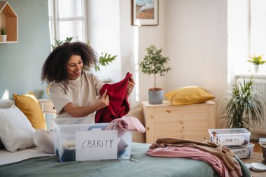 Evde gardırop düzenleyen mutlu genç bir kadın, bağış konsepti..