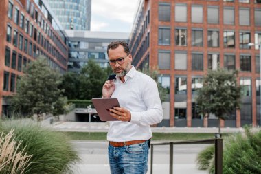 Modern ofis binasının önünde elinde tablet olan ve bir şeyler okuyan bir iş adamı..