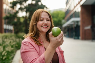 Artı yeşil elma tutan bir kadın, dışarıda oturuyor..