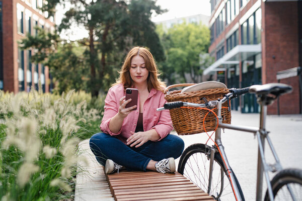 Женщина среднего роста отдыхает в общественном парке, держа в руках телефон.